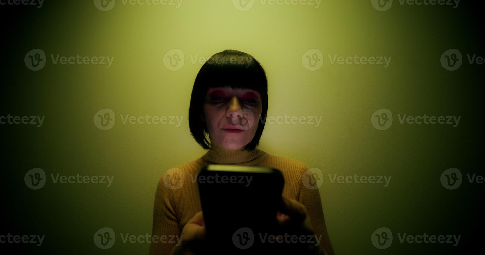 A woman in a wig uses a mobile phone, leaning against the wall in the orange backlight in the studio - backlight photo