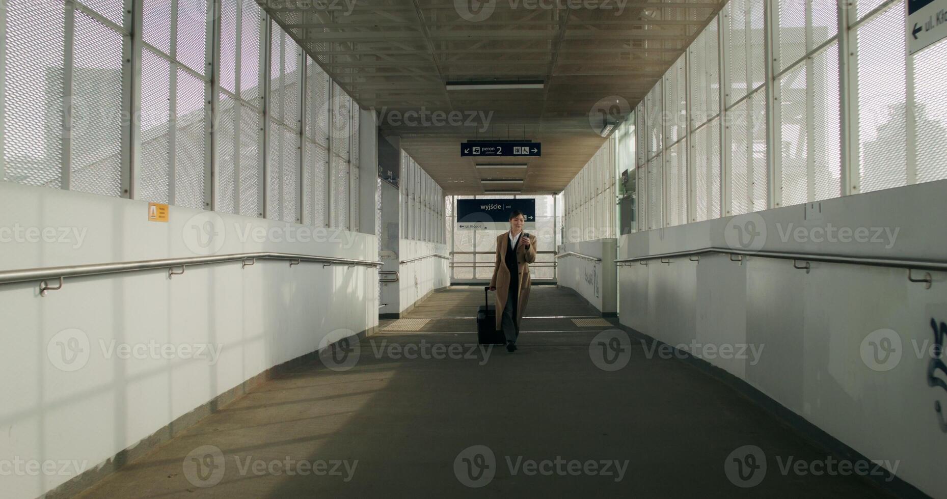 A woman in formal clothes and a coat uses a mobile phone walking along the corridor of the railway station - mobile photo