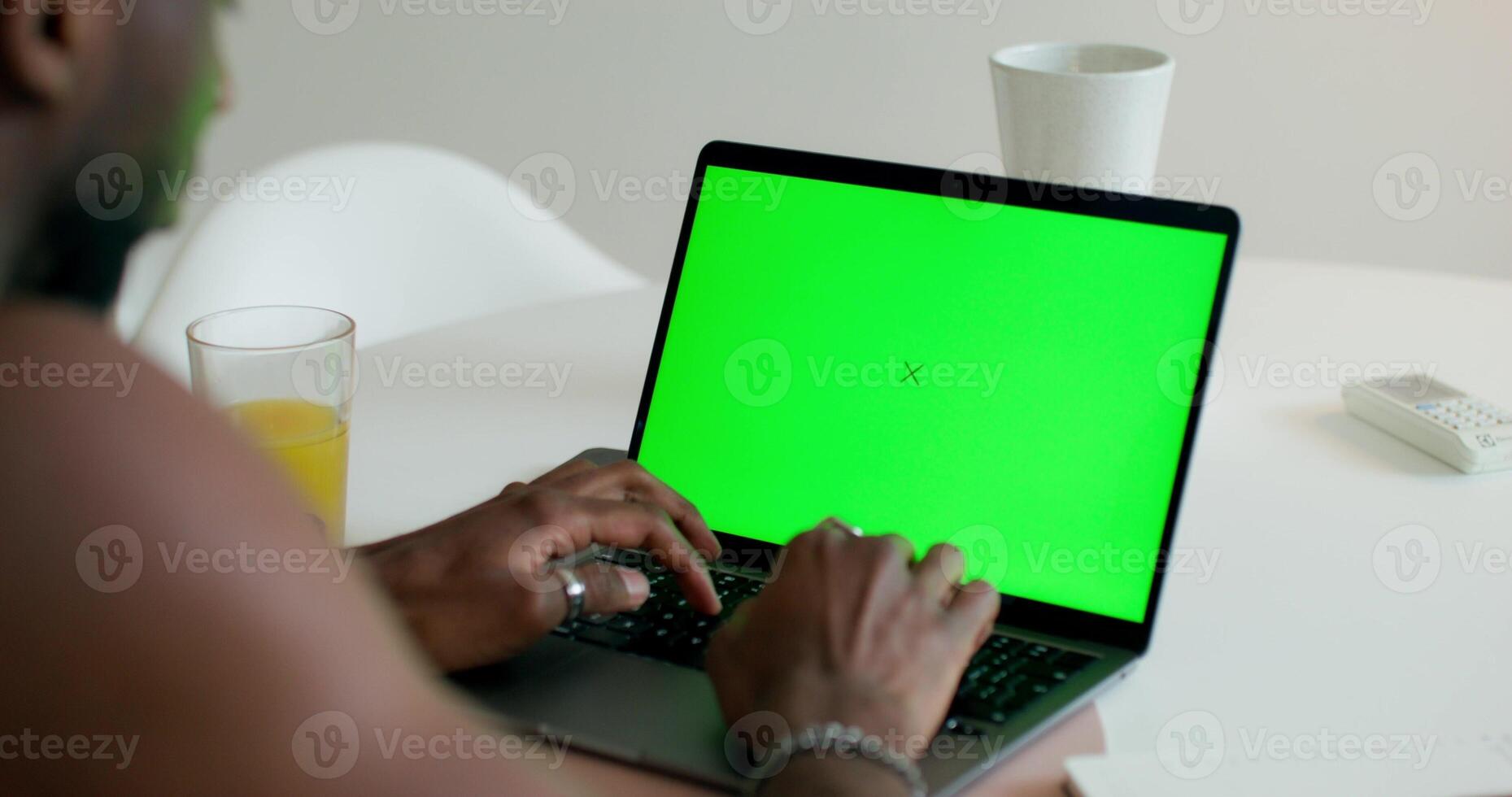 A man uses a laptop with a green screen sitting at a table at home, close-up of his hands, an unrecognizable person. Daylight photo