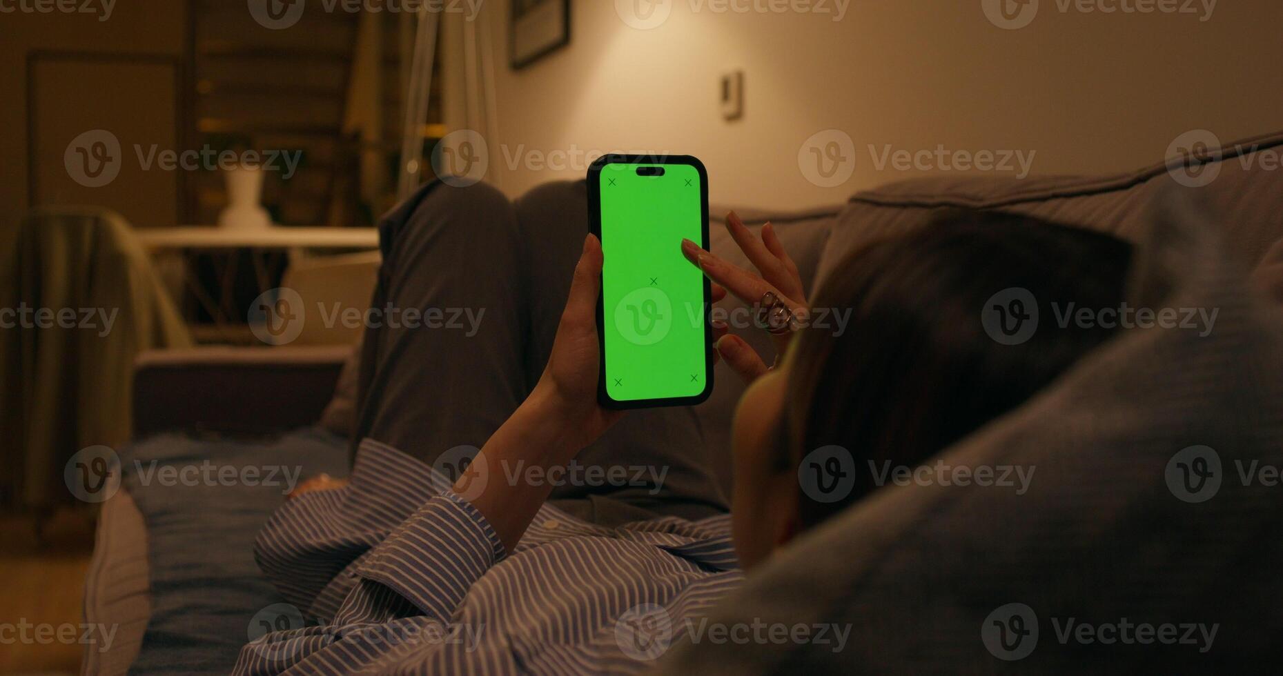 A woman uses a mobile phone with a green screen lying on the couch at home - mobile photo