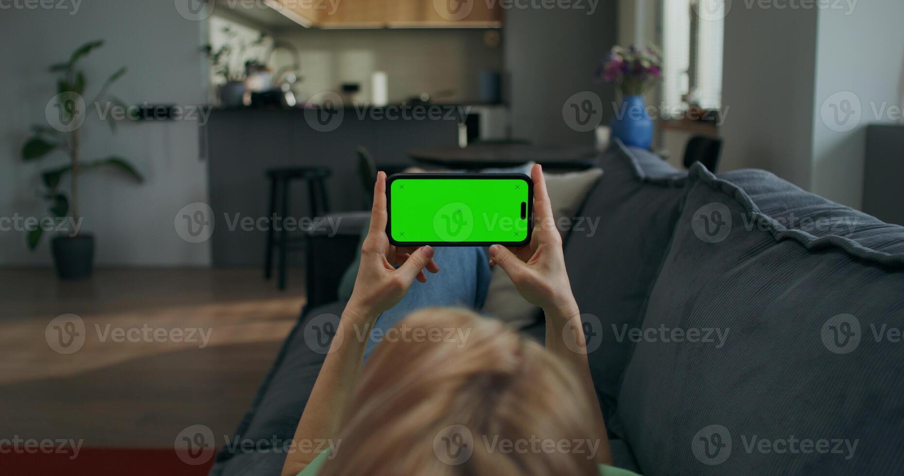 A woman holds a mobile phone with a green screen horizontally in her hands watching , rear view, an unrecognizable person - horizontally photo