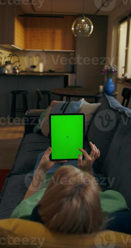 A woman uses a tablet with green screen lying on the couch at home, an unrecognizable person - tablet photo