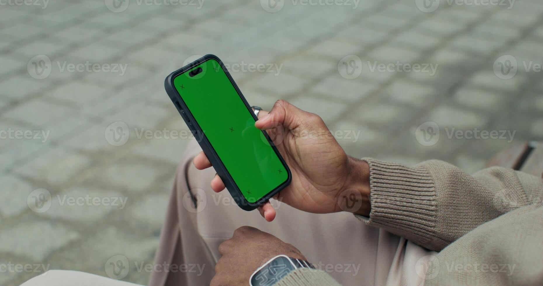 A man uses a mobile phone with a green screen sitting outdoors, close-up of his hands, an unrecognizable person photo