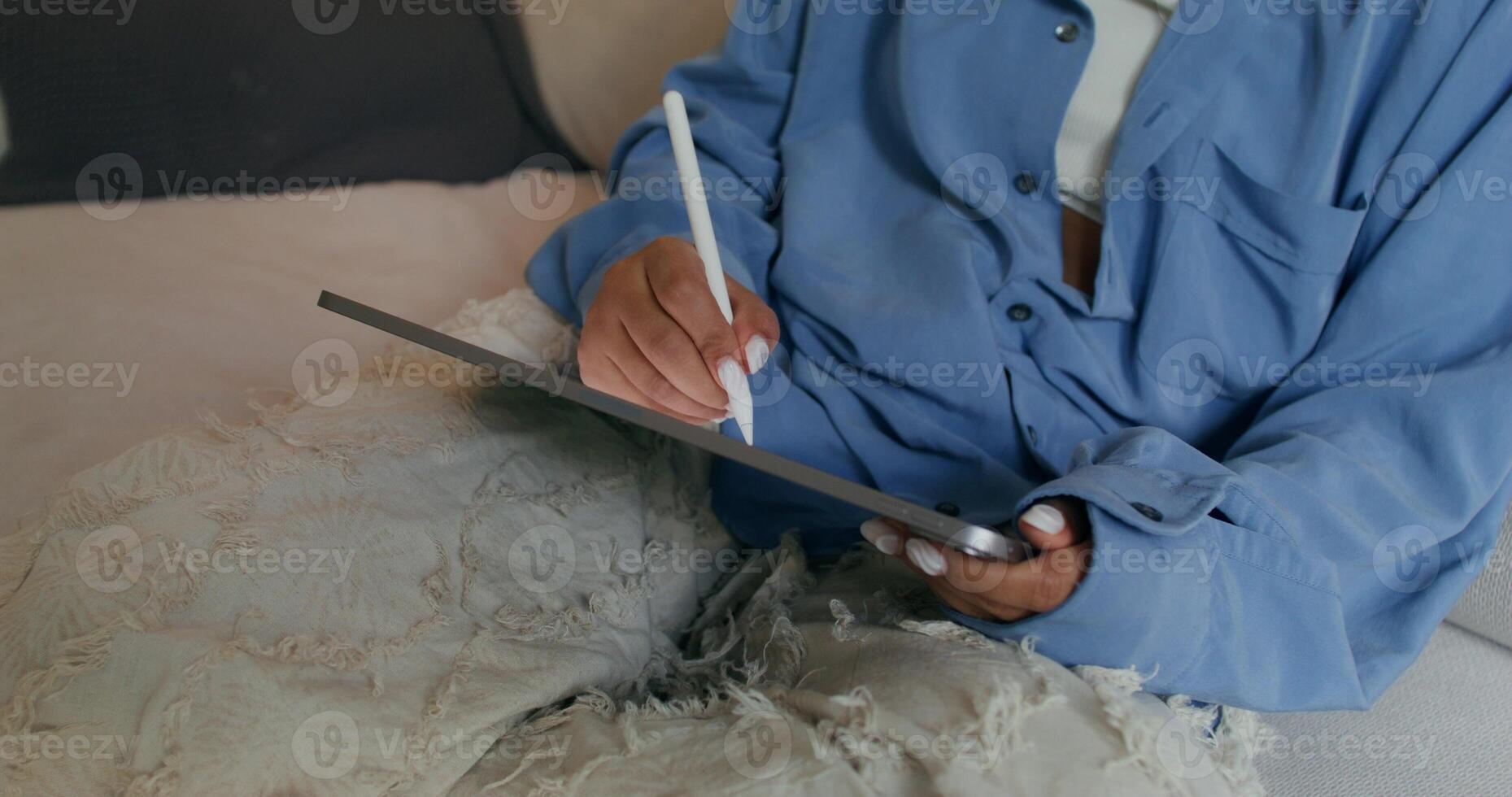 A woman uses a tablet sitting on the couch at home. She draws on it with a stylus. Close-up of her hands, an unrecognizable person - person photo