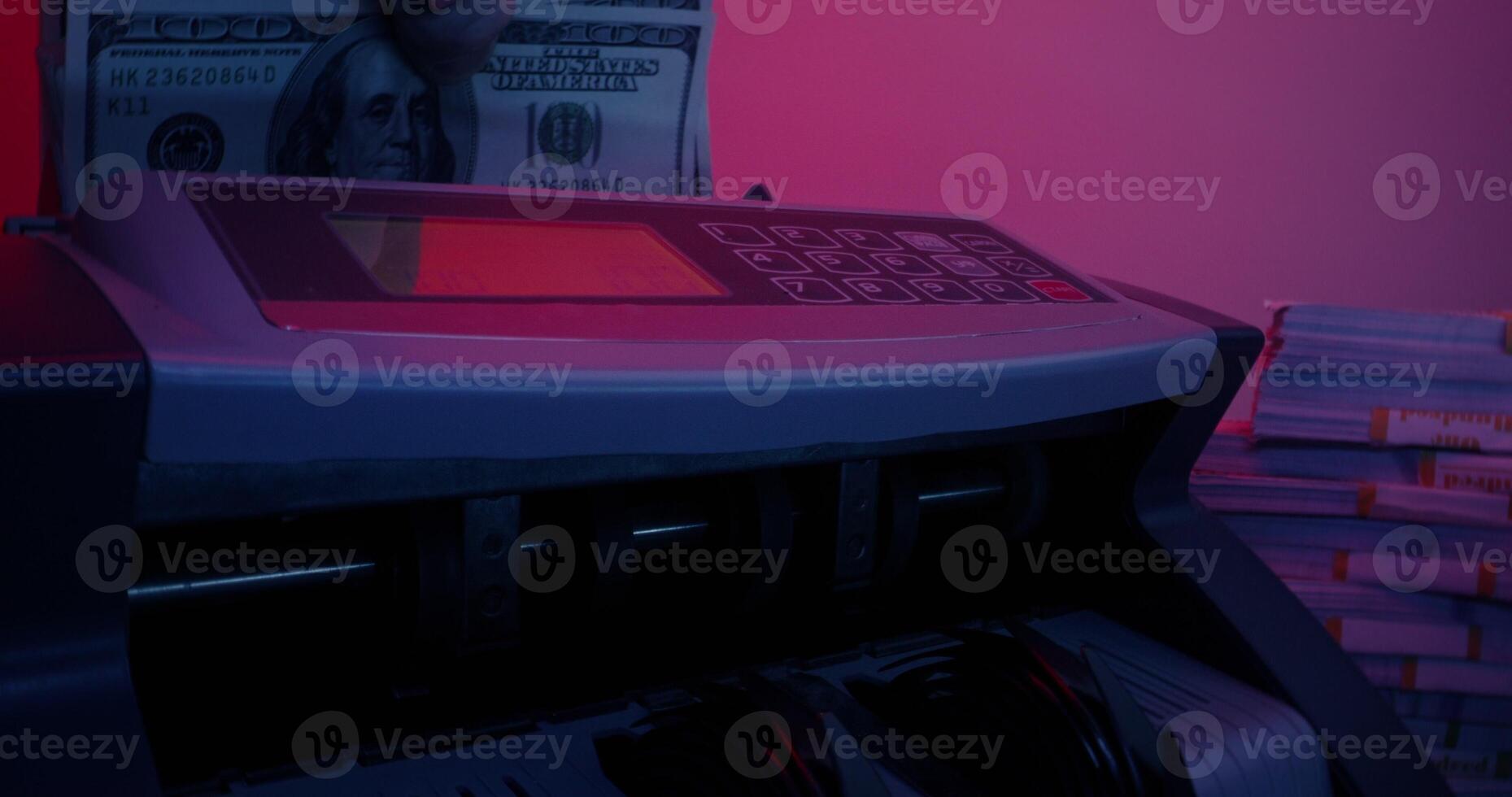 A man's hand with a ring inserts a stack of hundred-dollar bills into the counting machine and it starts counting. Bundles of money are lying around on the table - machine photo