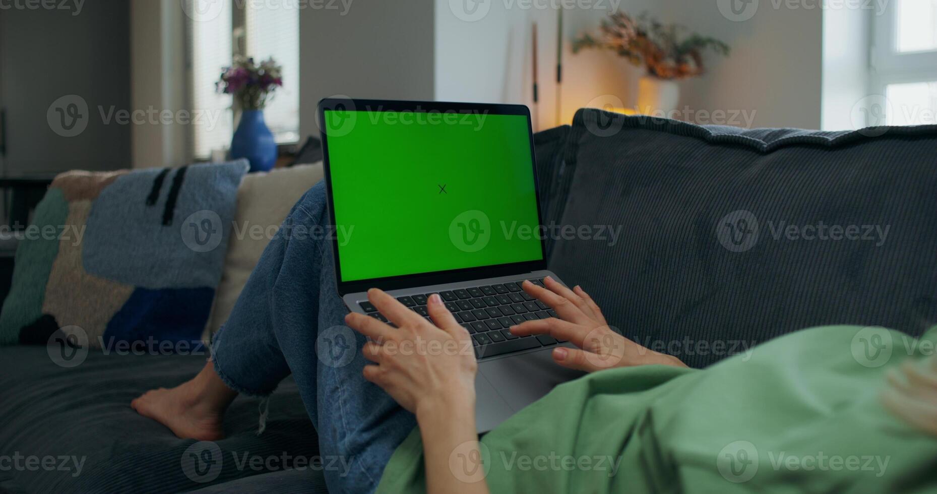 A woman uses a laptop with green screen lying on the couch at home, close-up of her hands, an unrecognizable person - person photo