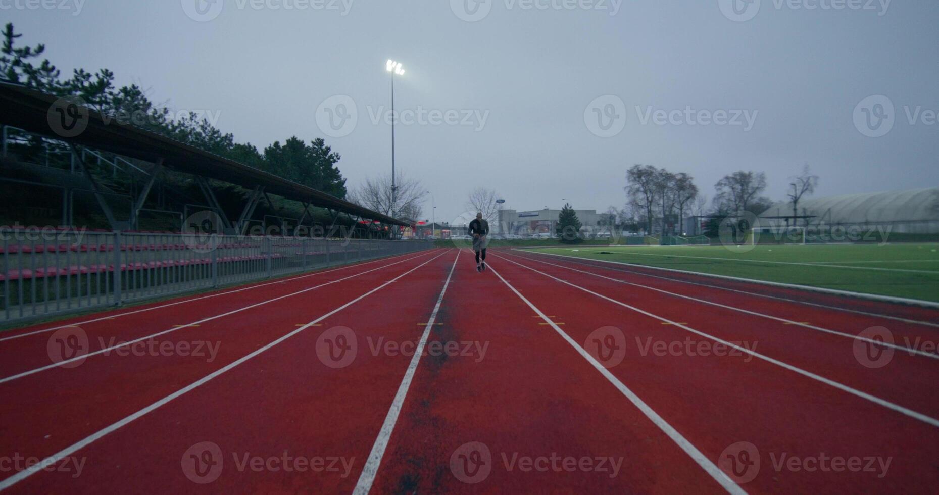 A man in sports clothes runs around the stadium on a cold day alone, front view - around photo