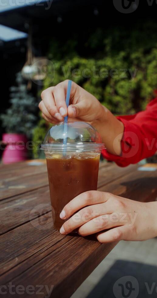 A disposable glass of lemonade is on the table, women's hands are stirring the drink with a straw - stirring photo