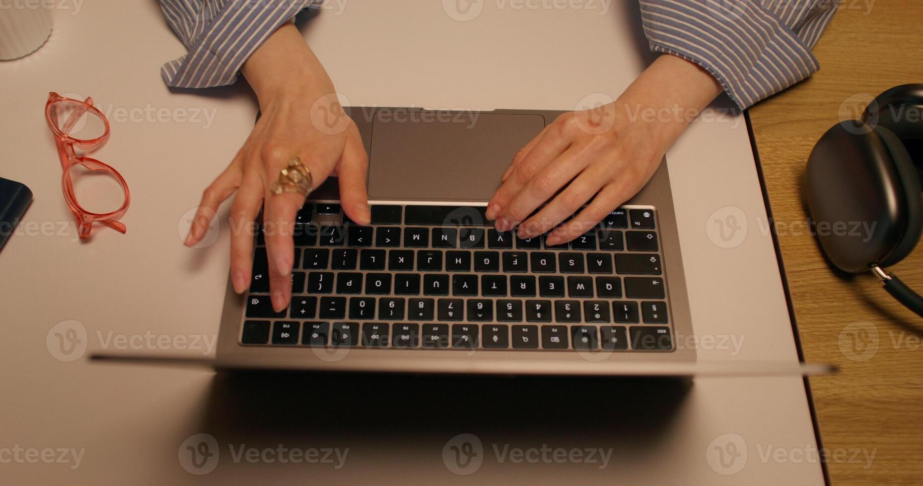 A woman typing on a laptop keyboard sitting at a table indoors, close-up of her hands, top view, unrecognizable person - keyboard photo
