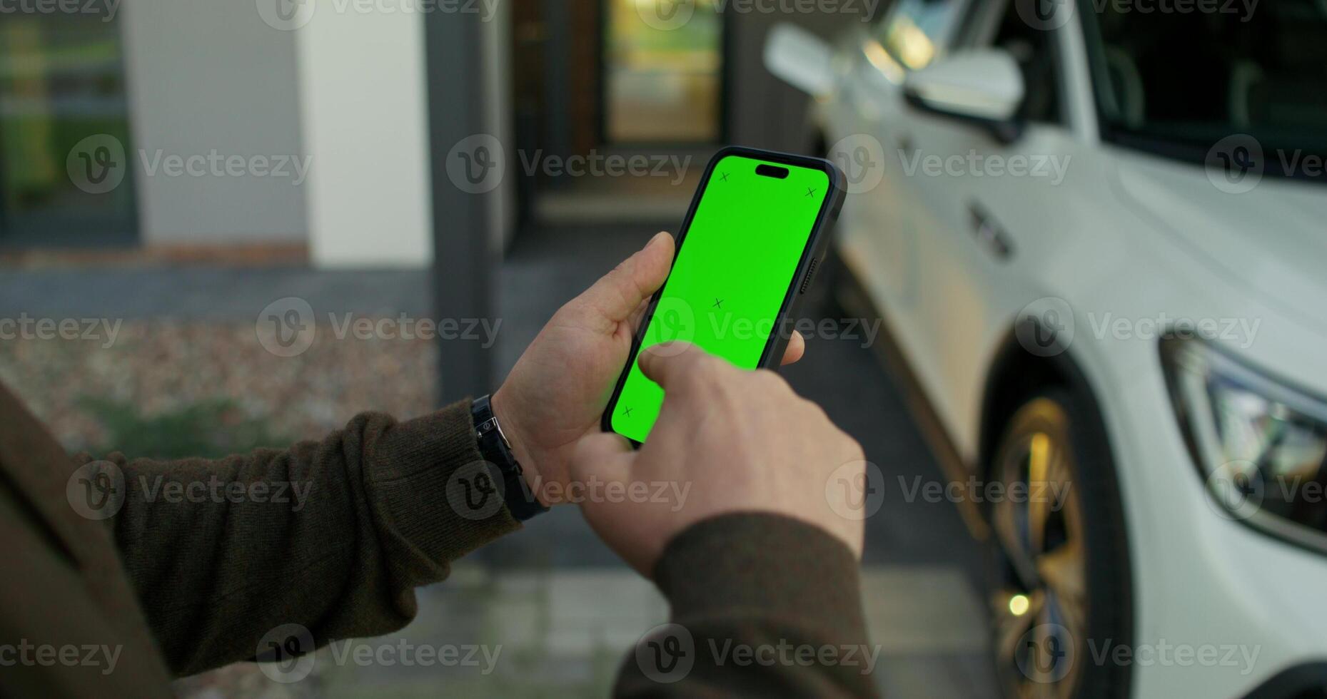 A man uses a mobile phone with green screen standing near an electric car. Close-up of his hands. - electric photo