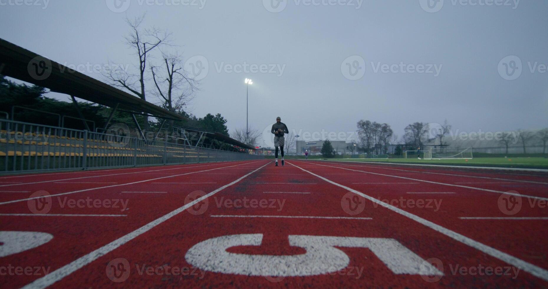A man in sports clothes runs around the stadium on a cold day alone, front view photo