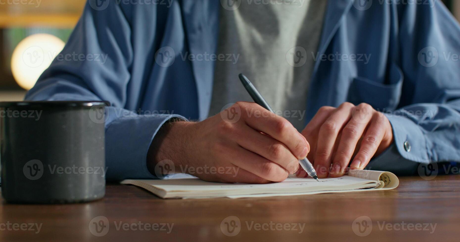 A man is writing in a notebook sitting at a table, close-up of his hands, an unrecognizable person - sitting photo