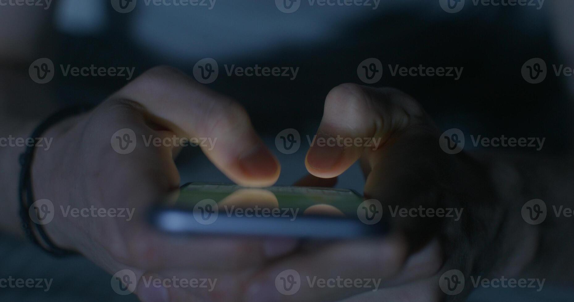 A man uses a mobile phone while sitting on the bed at night. Close-up of his hands, an unrecognizable person. Dark room, home interior - interior photo