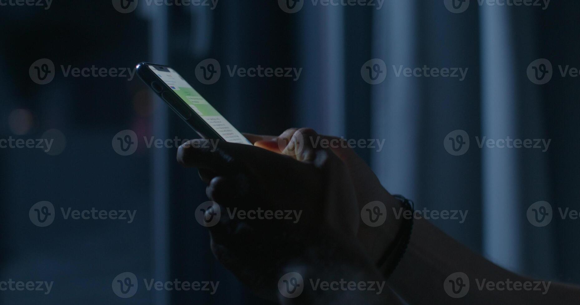 A man uses a mobile phone while sitting on the bed at night. Close-up of his hands, an unrecognizable person. Dark room, home interior - mobile photo