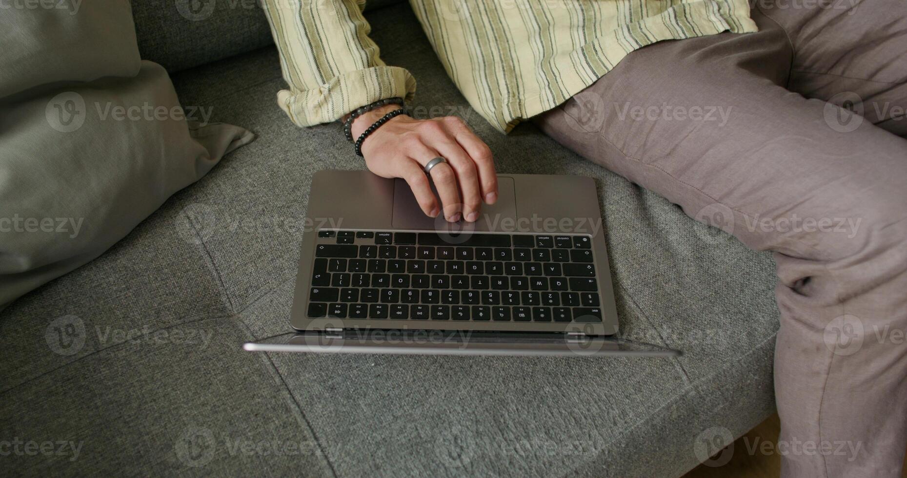 A bearded man uses a laptop and talks on a mobile phone sitting on the couch at home with a serious look. Daylight - mobile photo