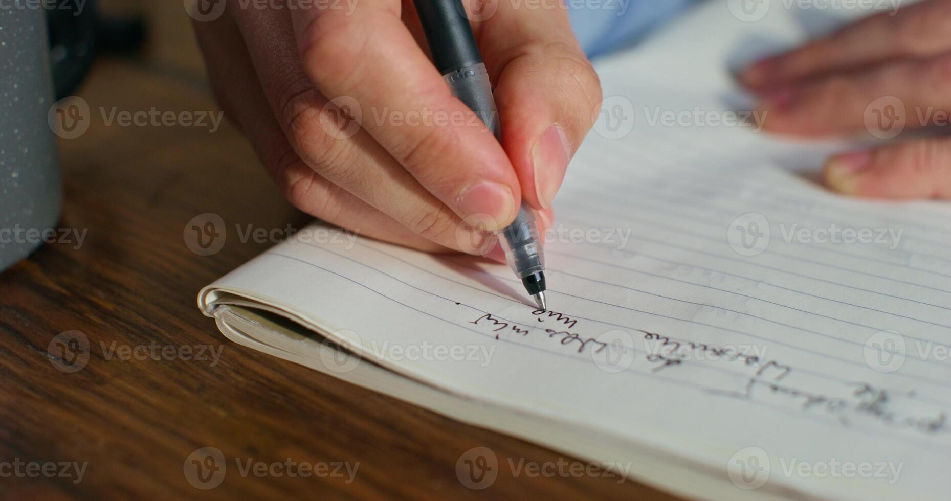 A man is writing in a notebook sitting at a table, close-up of his hands, an unrecognizable person photo