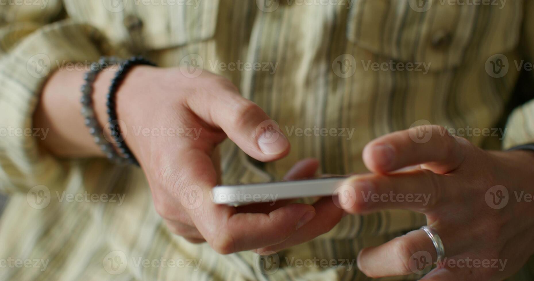 A man is typing on a mobile phone sitting on the couch at home. close-up of his hands, an unrecognizable person. Daylight photo