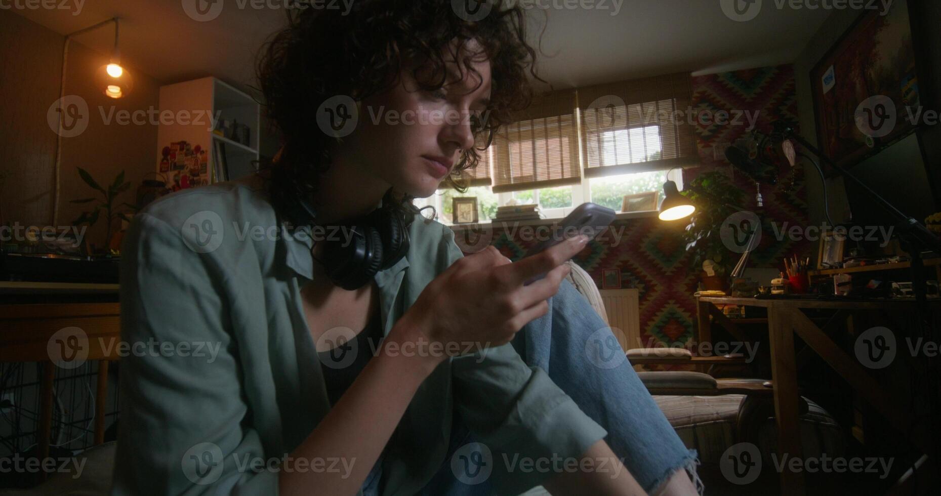 A young woman uses a mobile phone while sitting on a bed at home with a depressed look - depressed - woman photo
