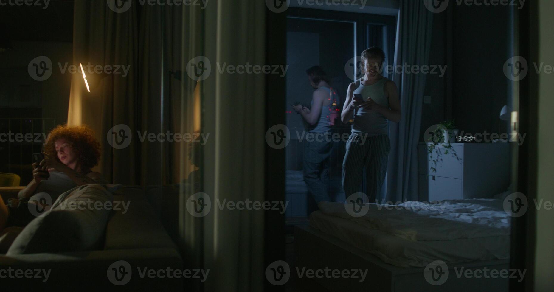 A woman uses a mobile phone sitting on the couch at home. The man throws the phone on the bed and lies down. He's upset. Home interior, night photo