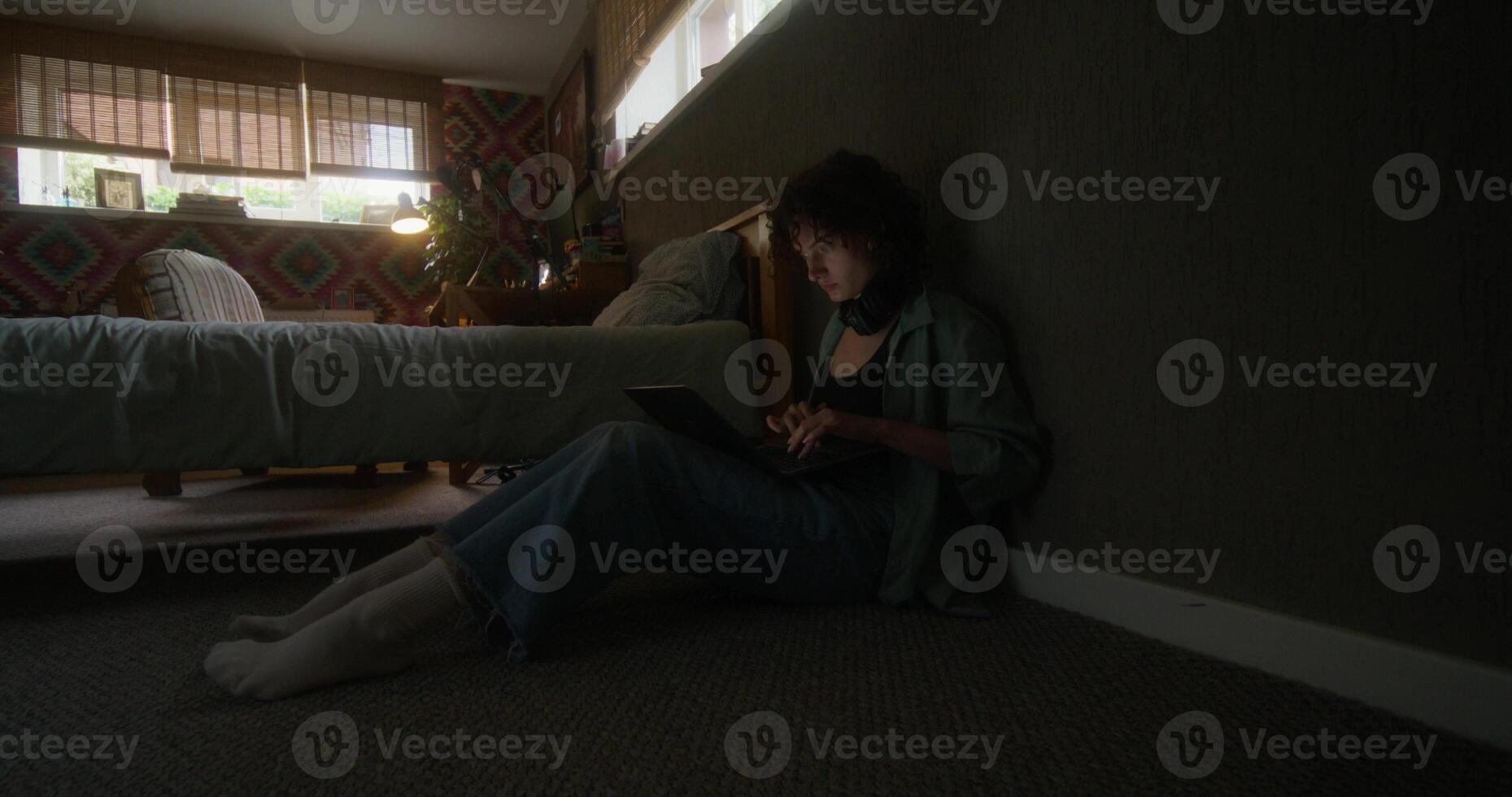 A young woman uses a laptop sitting on the floor in the bedroom at home with a serious look photo