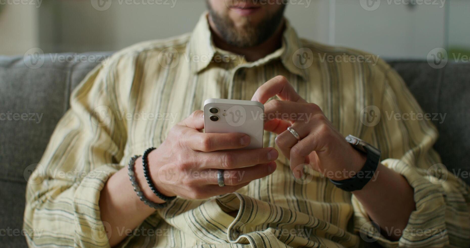 A man is typing on a mobile phone sitting on the couch at home. close-up of his hands, an unrecognizable person. Daylight - sitting photo