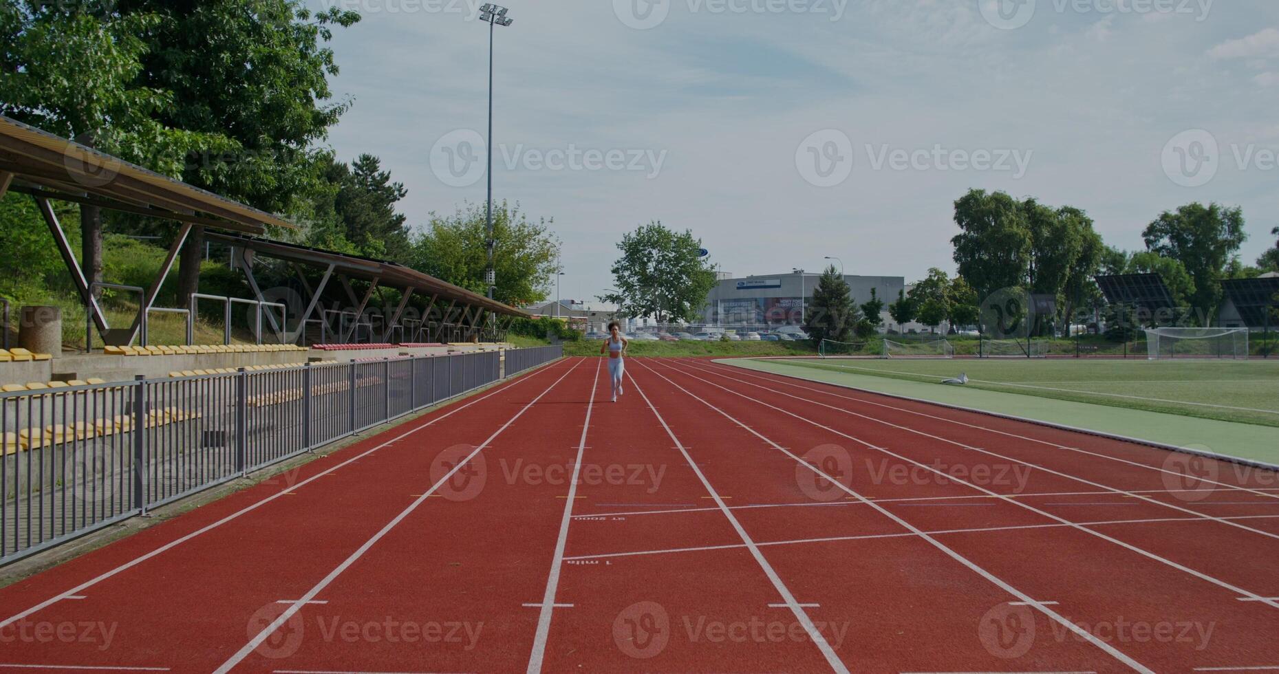 A woman in sports clothes and with earphones in her ears runs at the stadium on a summer day - sports photo