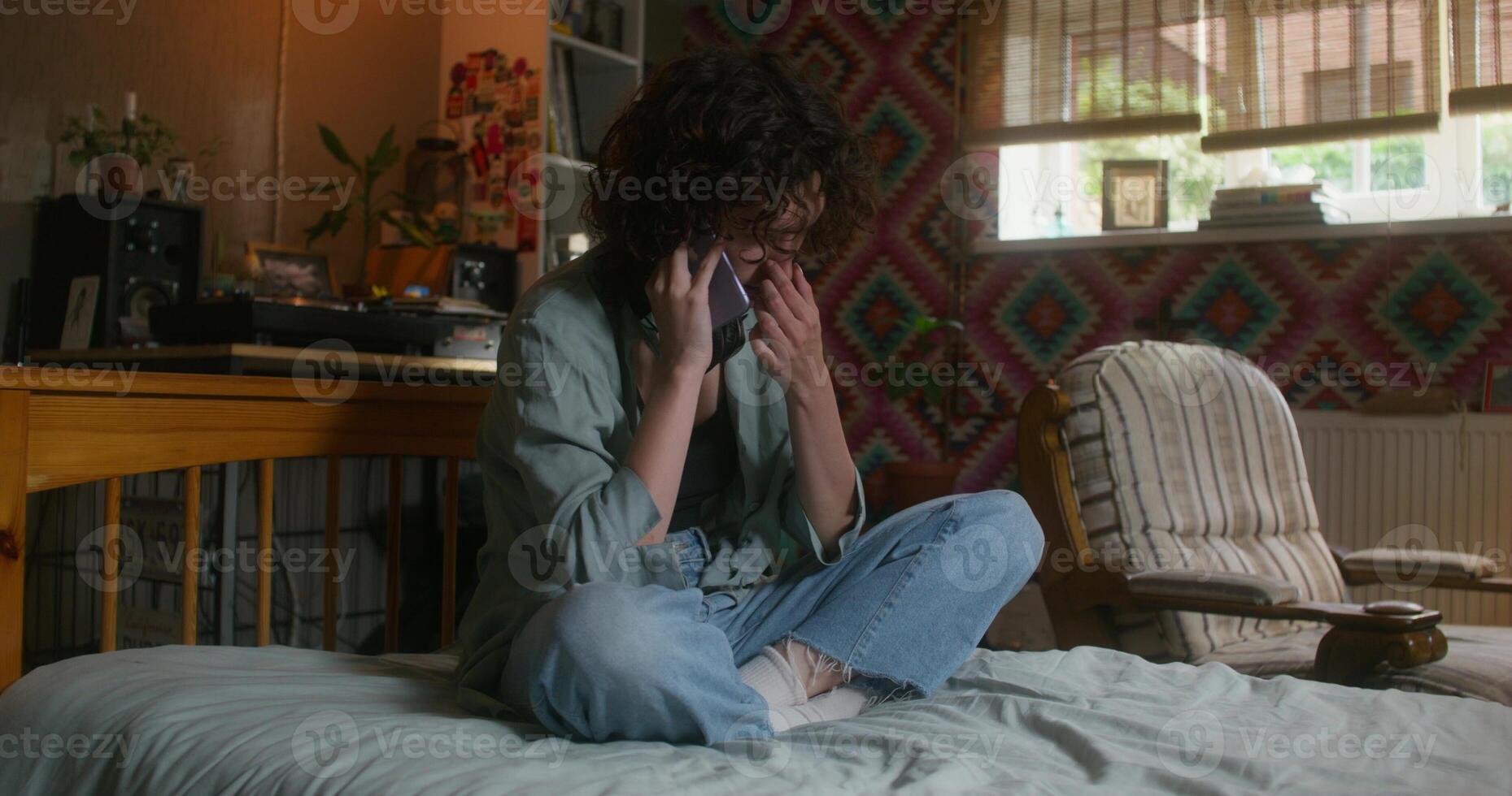 A young woman is talking on a mobile phone sitting at home with a sad look - talking photo