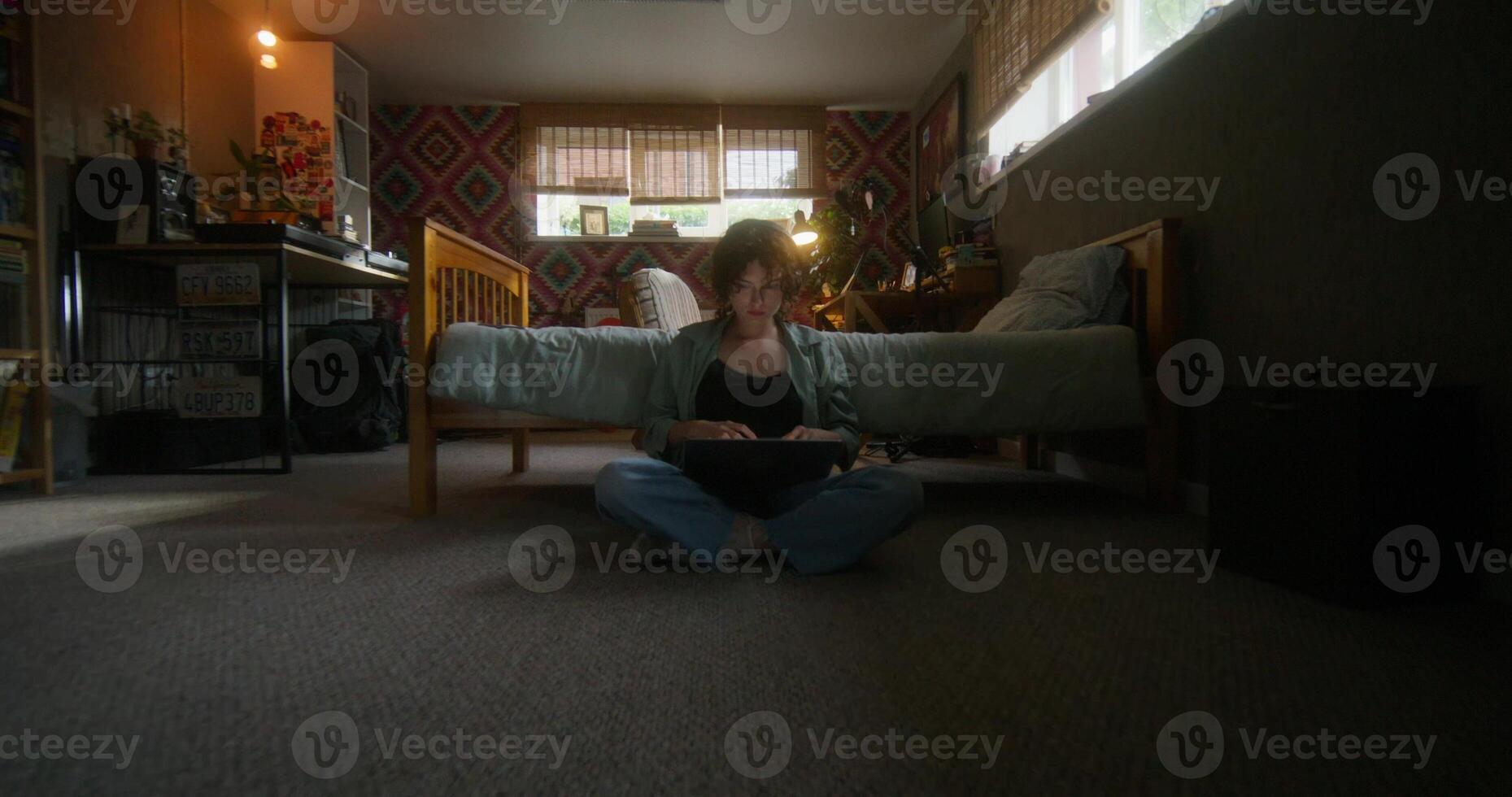 A young woman uses a laptop sitting on the floor in the bedroom at home with a serious look - bedroom photo