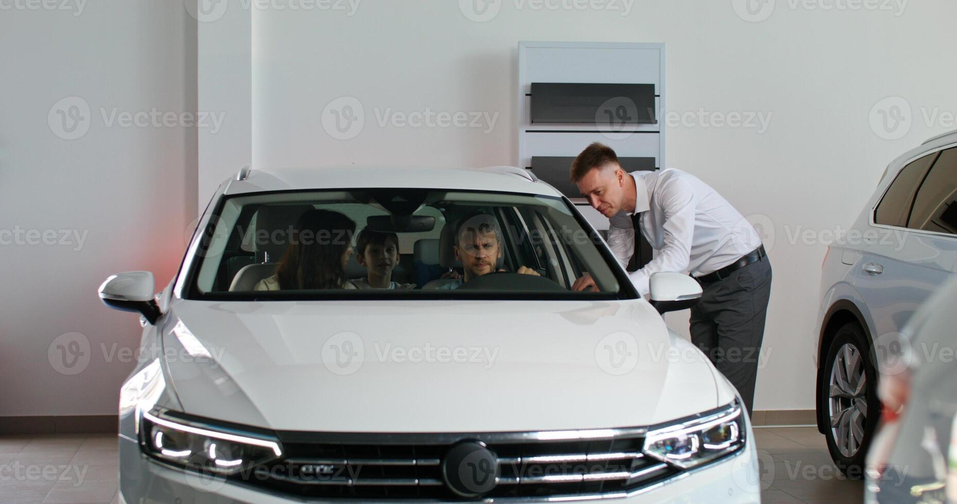 A man and woman are looking at a car in a showroom photo