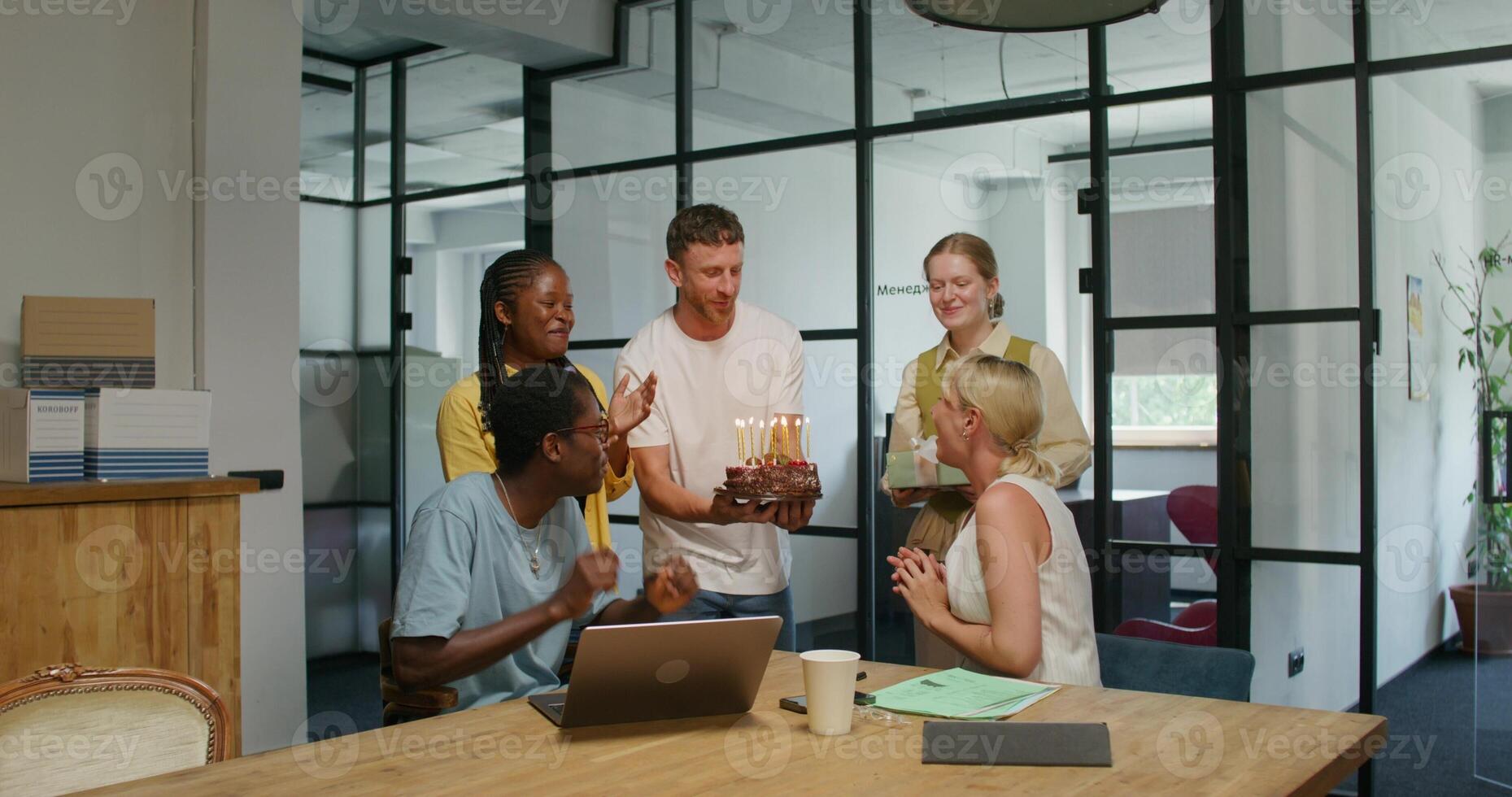 Colleagues wish a woman a happy birthday in the office. She blows out the candles on the cake. Daylight - candles photo