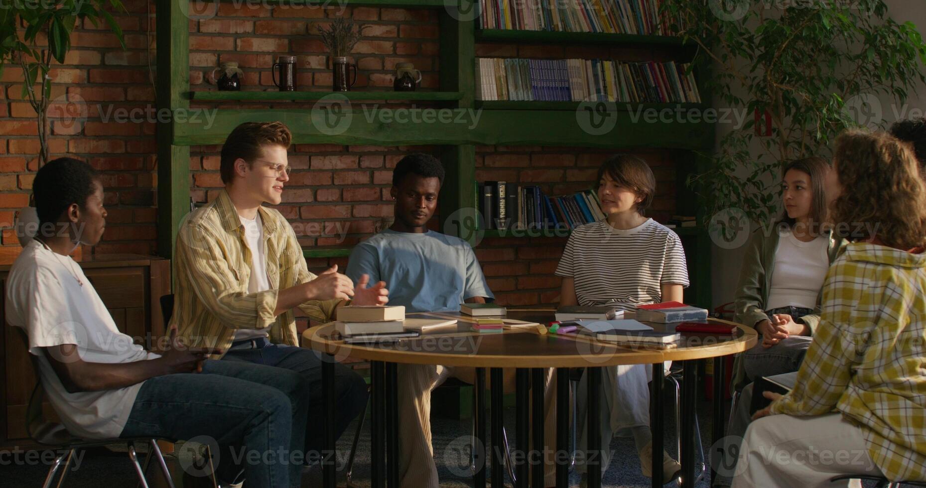A man is talking to his friends while sitting at a table indoors. He opens the Bible. Bible Study Club photo