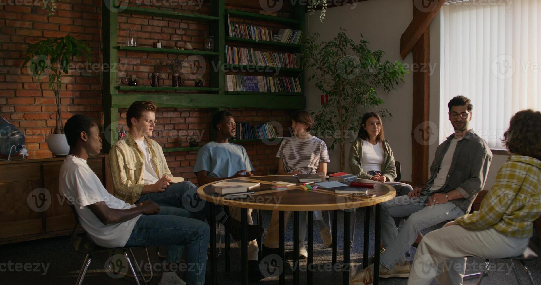 Bible Study Group. Young people talk in pairs while sitting at a table indoors. The books are on the table. Daylight photo