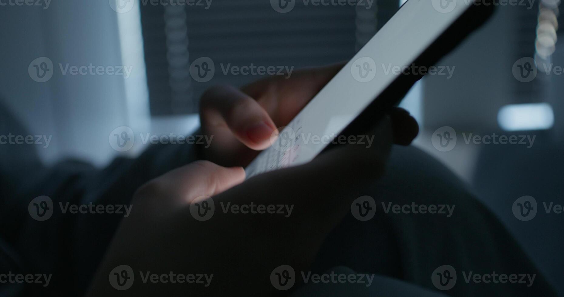 A woman uses a mobile phone while sitting in a dark room. Close-up of her hands, an unrecognizable person photo