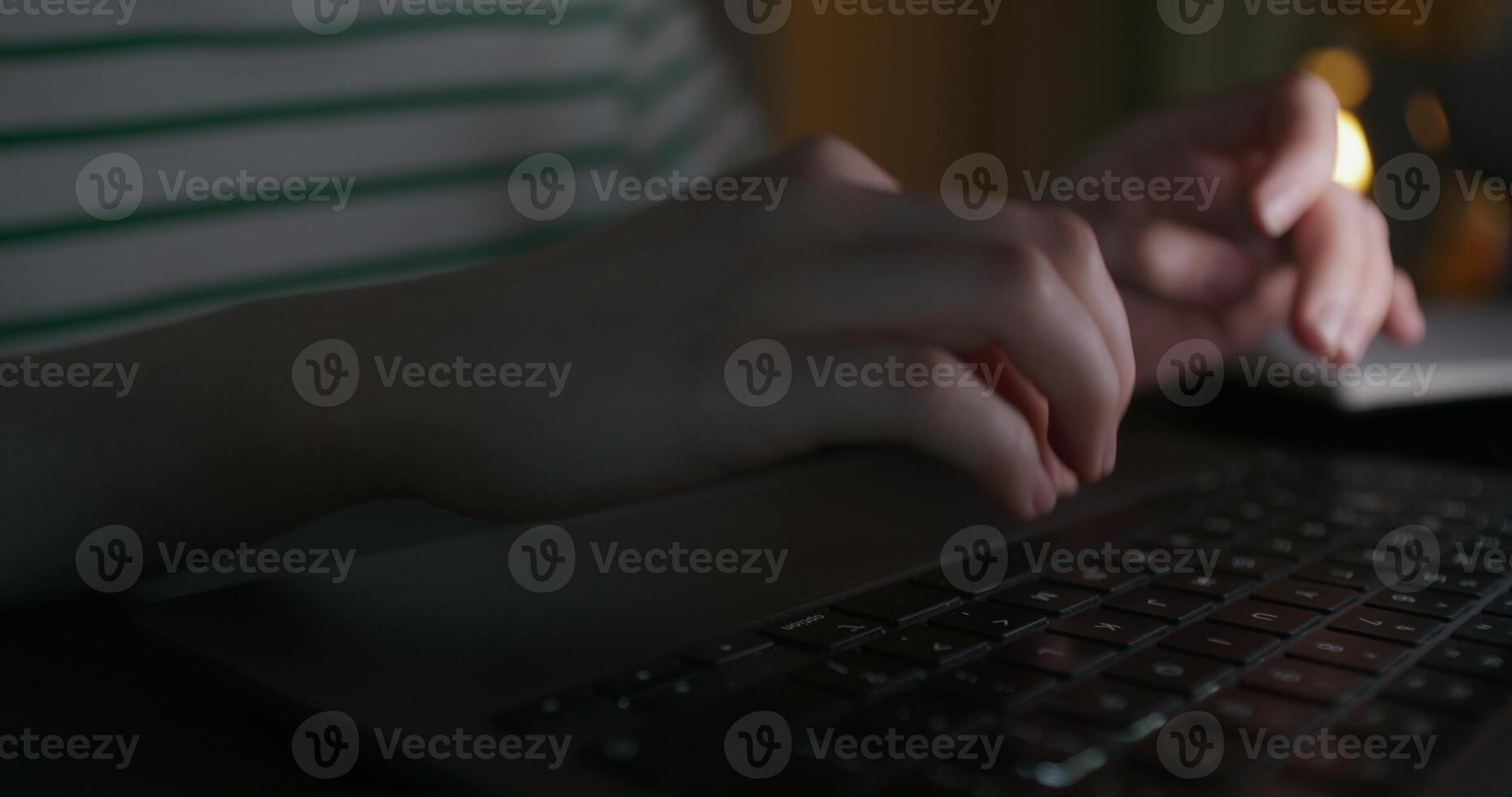 A woman typing on a laptop keyboard while sitting at a table in the dark. Close-up of her hands, an unrecognizable person. - keyboard photo