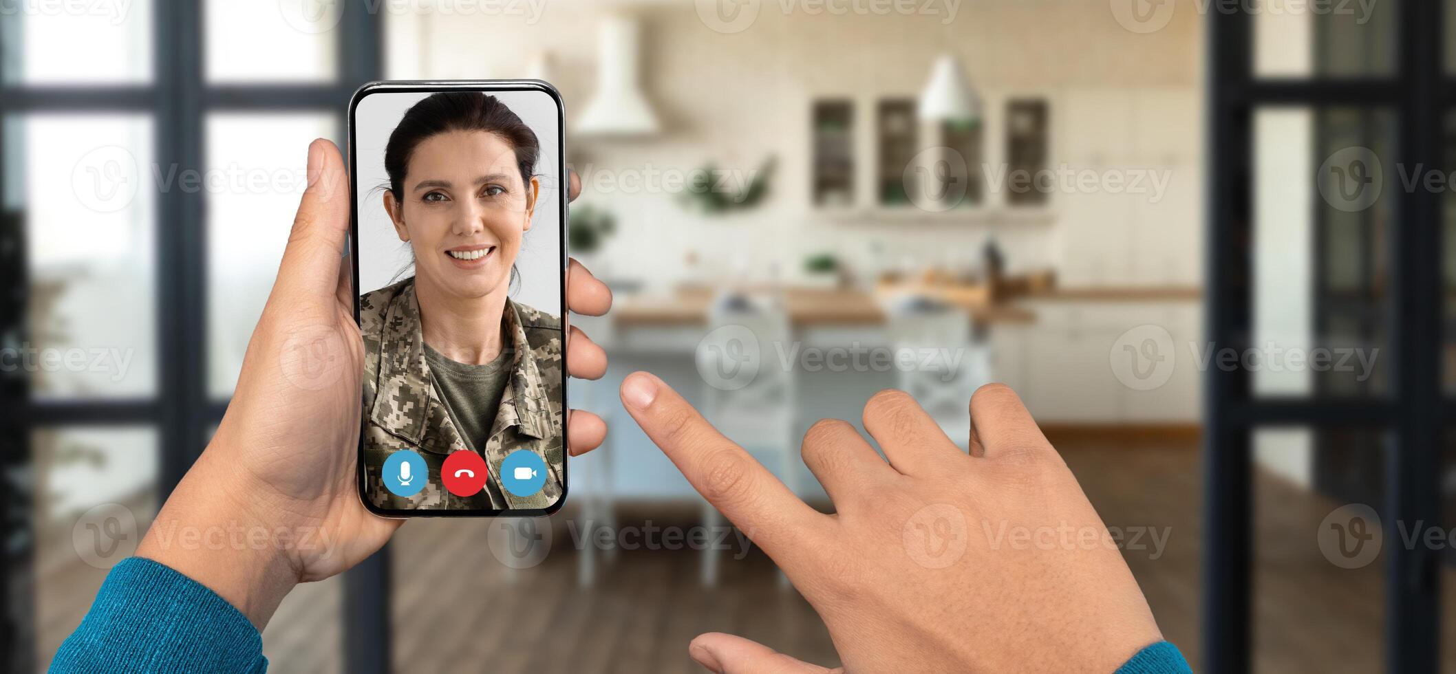 A person is using a smartphone to connect with a friend through a call. The home setting features a modern kitchen, and the focus is on communication and connection. photo