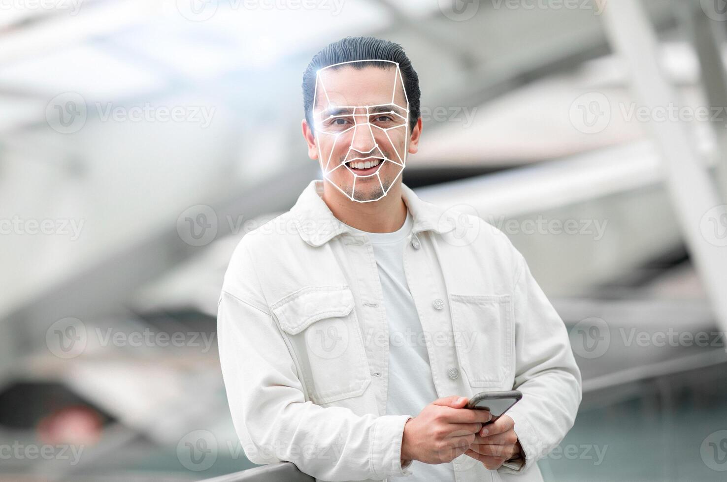A young man stands confidently with a smartphone in hand, engaging with advanced facial recognition technology in a contemporary urban setting. This reflects the new normal of digital identification. photo