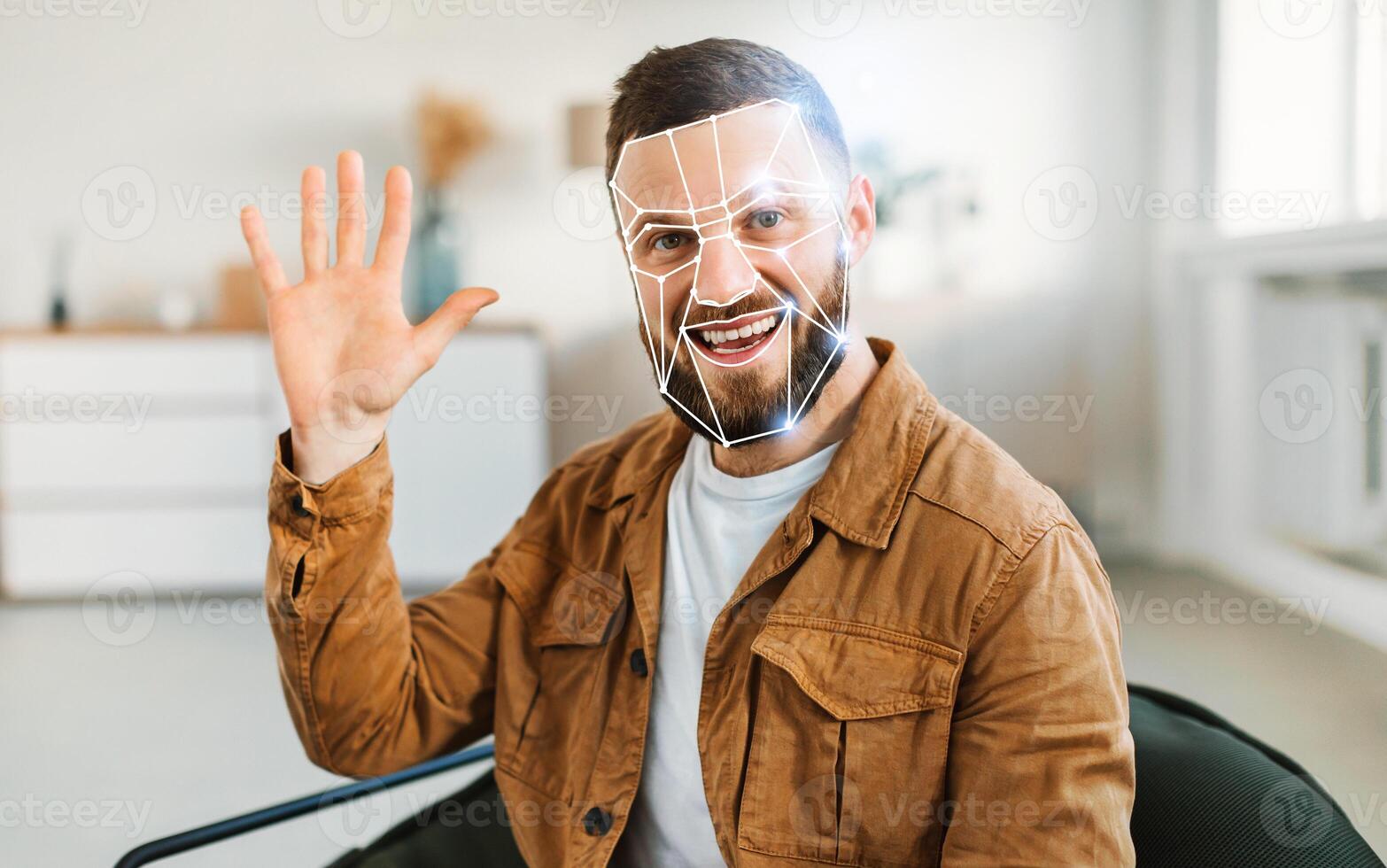 A man waves while sitting in a contemporary office, showcasing facial recognition technology. The room is bright and minimalistic, reflecting a modern approach to identification. photo