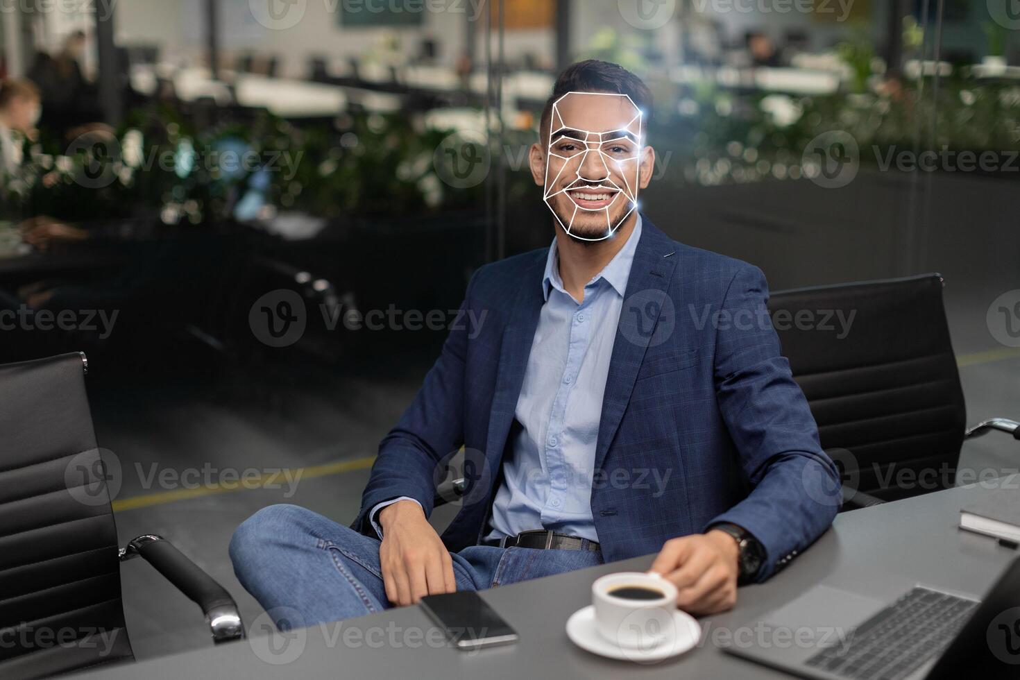 A man dressed in business attire sits comfortably at a conference table, using facial recognition technology for identification while enjoying a cup of coffee in a contemporary office environment. photo