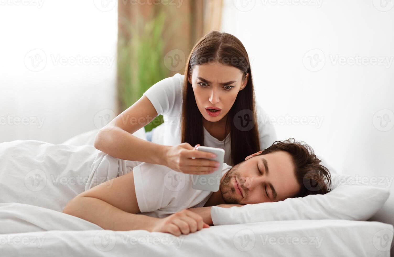 Infidelity. Shocked Wife Reading Message From Lover On Phone While Cheating Husband Sleeping In Bedroom At Home. Jealous Woman Checking Boyfriend's Cellphone Chats. Affair, Relationship Issues photo