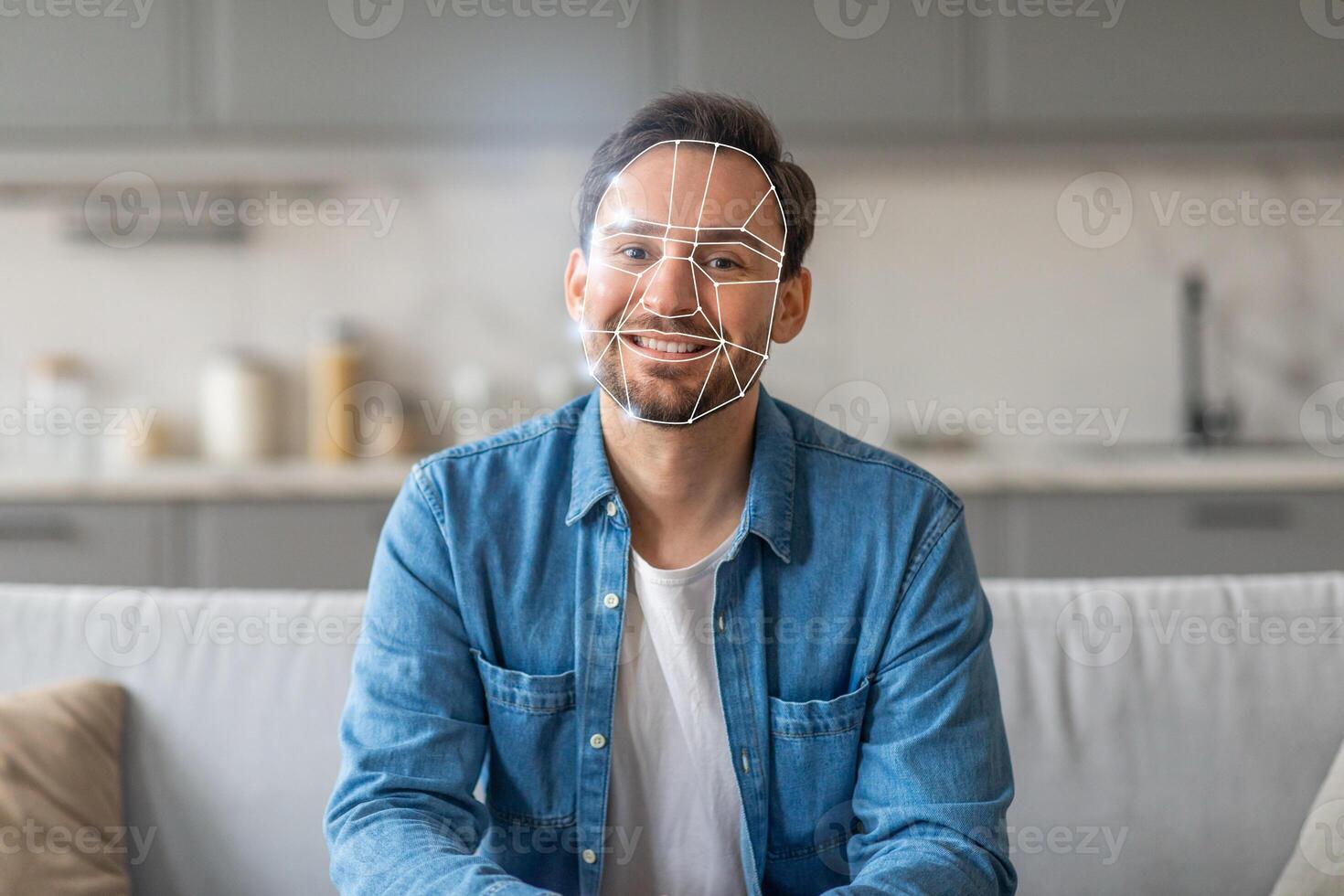 A man smiles while sitting on a couch in a contemporary kitchen, where facial recognition technology is being used to verify his identity. The modern design reflects a new normal in tech. photo