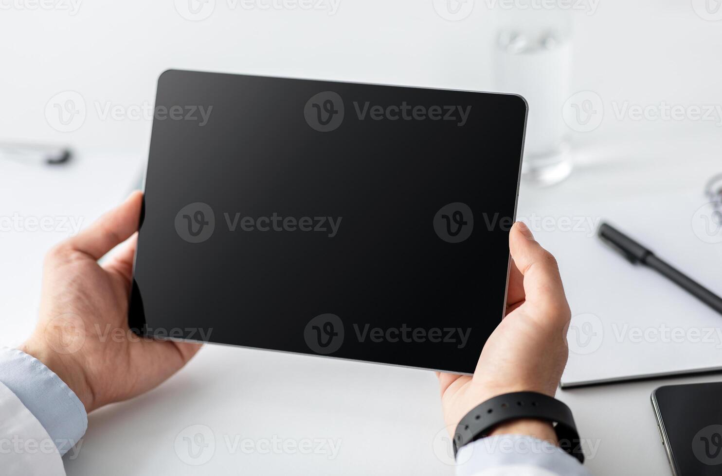 Online digital touch screen with ad, offer and website or medical blog. Young businessman or doctor in coat with smart watch uses tablet with blank screen on white table with notepads, close up photo
