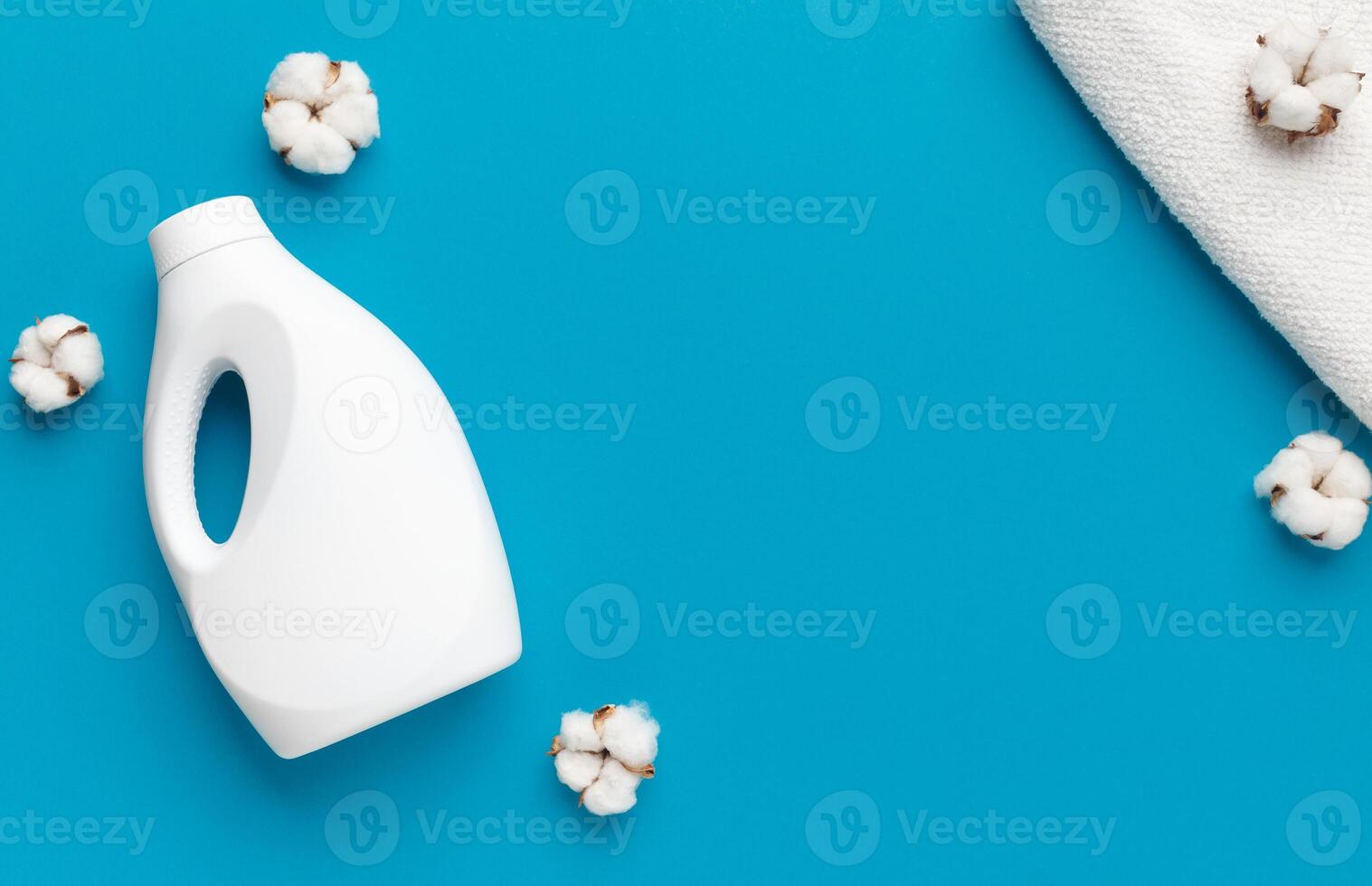 Eco washing concept. White plastic packaging of laundry detergent, cotton flowers and white soft towel on blue background, copy space photo