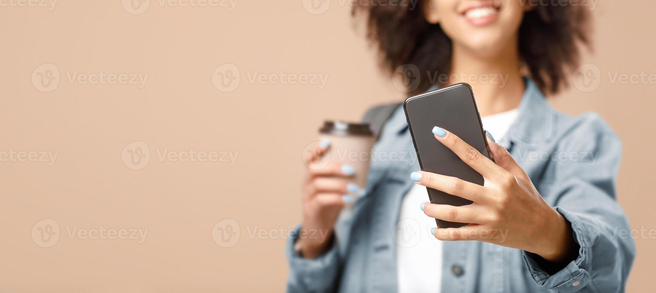 Millennial, modern lifestyle and photo for blog after quarantine. Happy african american lady with smart watch and cup of coffee makes selfie on smartphone, isolated on yellow background, panorama