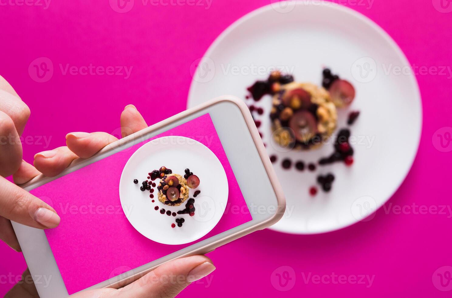 Top view close-up of female hands making flat lay food photo with phone for restaurant menu or social network. Oatmeal porridge on pink background, mockup, template, copy space, shallow depth of field