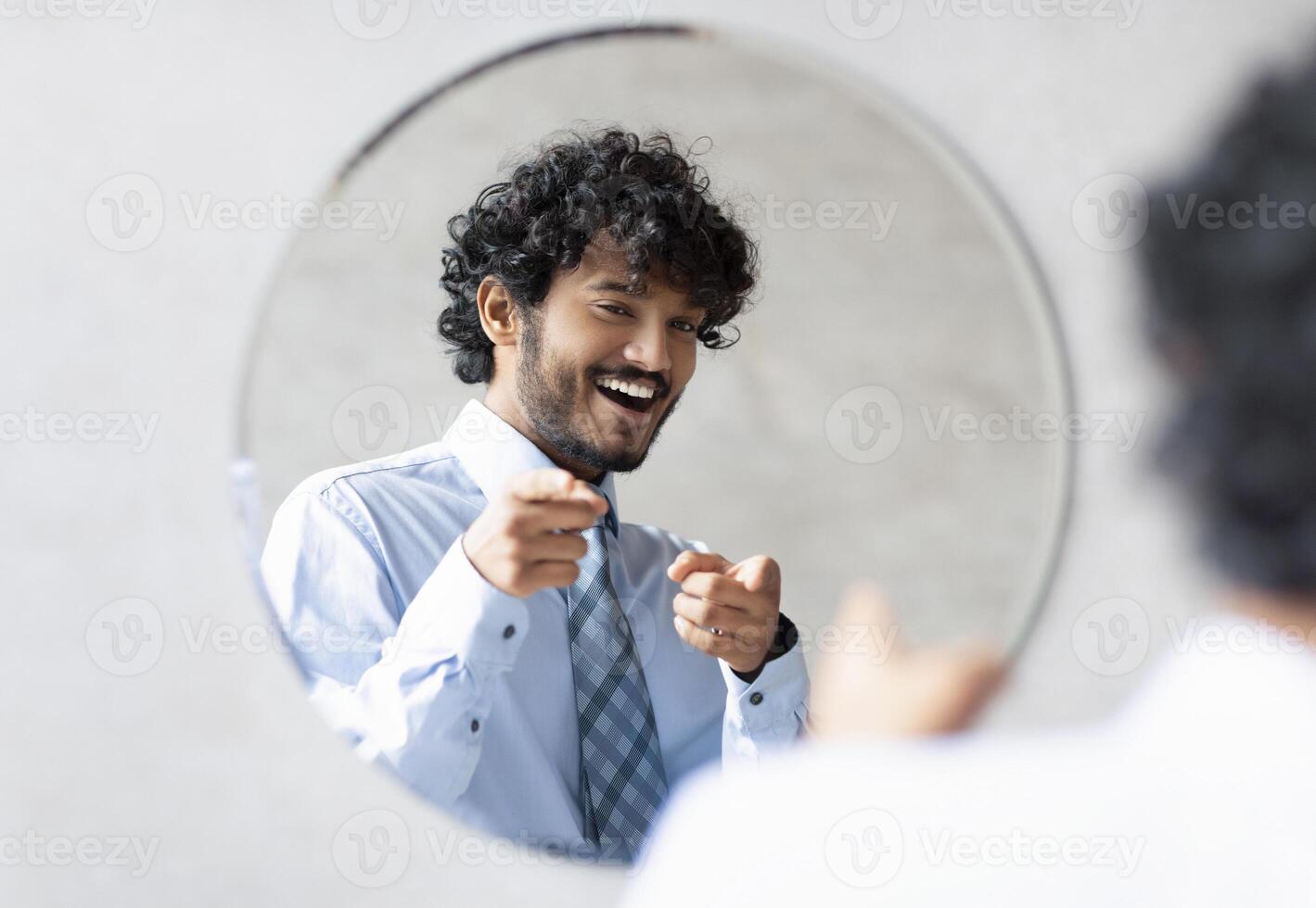 You're handsome. Confident indian businessman pointing at mirror in bathroom with two fingers, man wearing shirt and smiling to his reflection, free space photo