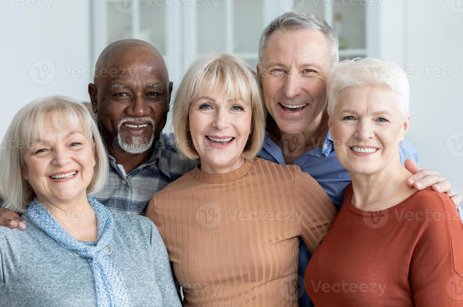 Portrait of multiracial group of happy senior friends men and women in casual outfits enjoying time together, cheerfully smiling at camera, kitchen interior. Elderly people lifestyle photo
