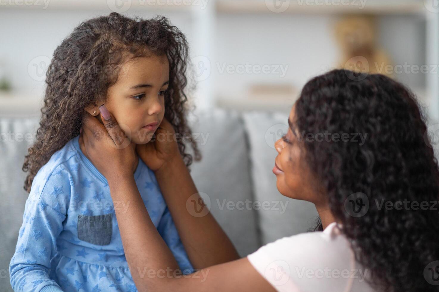 Family misunderstanding, childhood problems concept. Young black mother comforting her sad offended daughter after quarrel at home. African American woman calming down her child photo