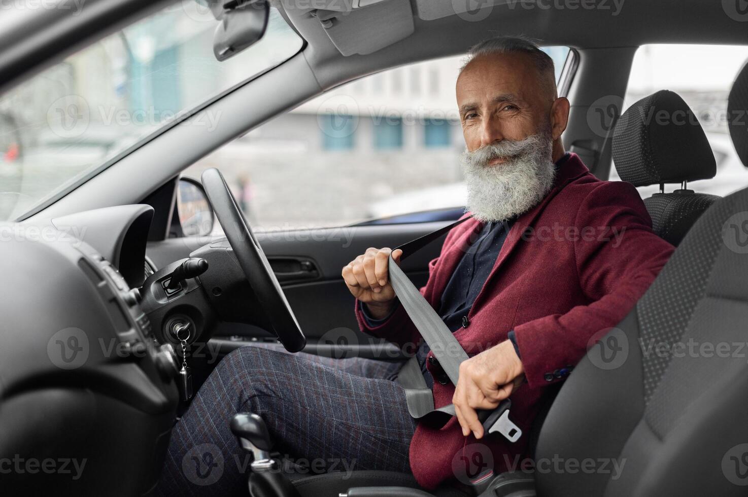 Driving safety concept. Senior businessman fasten seat belt in his car, ready to go to office. Aged man in stylish suit putting on his seatbelt before driving car to airport, copy space photo