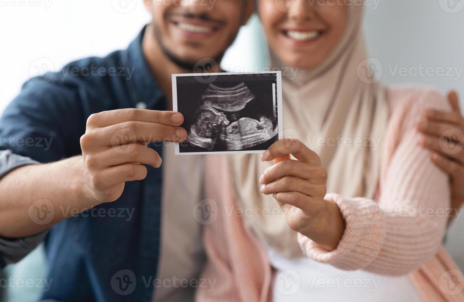 Closeup shot of happy pregnant muslim couple demonstrating baby sonography photo while relaxing together at home, showing first photo of their child, enjoying future parenthood, cropped image