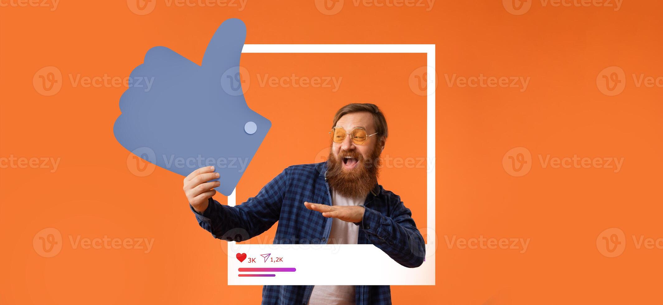 A man with a beard and glasses celebrates his success by making a thumbs up gesture while engaging with his online audience. The bright orange background enhances his joyful expression. photo